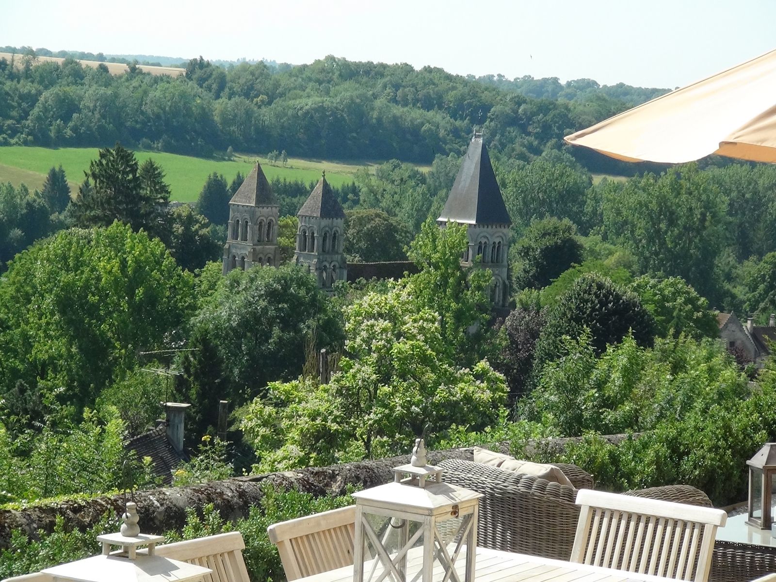 La terrasse de L’Instant La Vue en plein été, la vallée et les clochers de l’abbaye romane au fond
